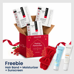 Innate Beauty 'Festive Favourites' hair care gift set featuring a red box filled with white and black hair treatment tubes, a red plush bow hair band, a red towel, and Aquataica moisturizer and sunscreen, with a pomegranate and ribbon on a white background.